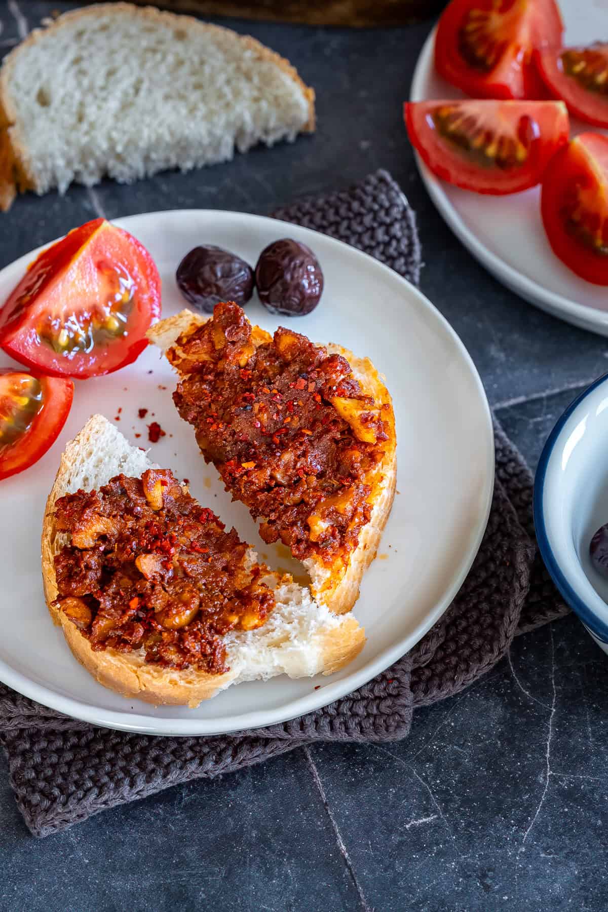 Acuka spread on slices of bread, served with tomatoes and olives as part of a traditional Turkish breakfast.