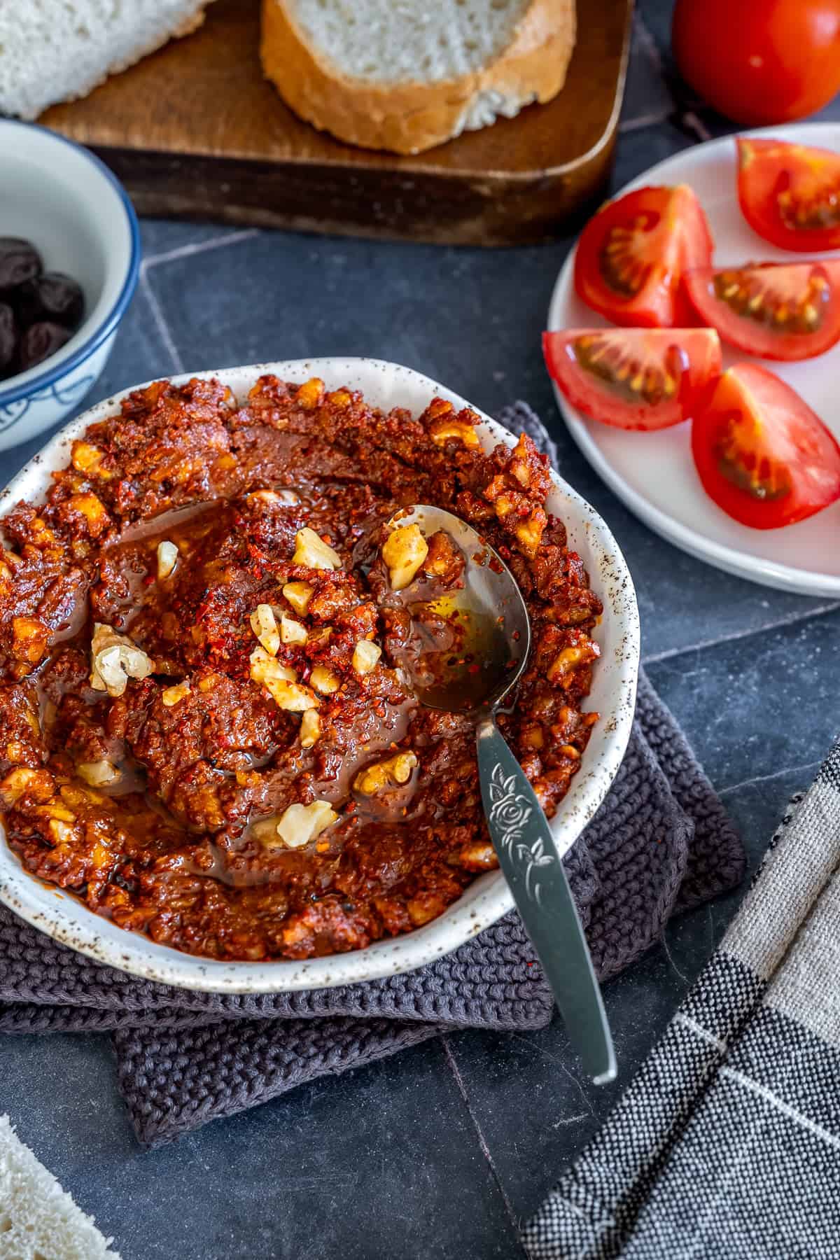 Close-up of acuka, a Turkish breakfast spread made with walnuts, tomato paste, pepper paste, garlic and spices, served with bread, olives and fresh tomatoes.