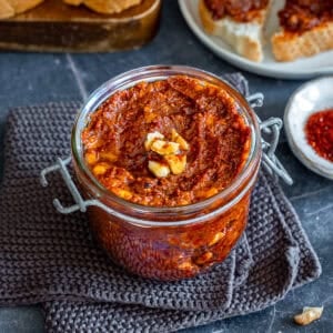 Jar of homemade acuka, a savory Turkish breakfast spread made with walnuts, tomato paste, pepper paste, garlic and spices, served with slices of bread.