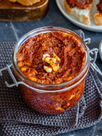 Jar of homemade acuka, a savory Turkish breakfast spread made with walnuts, tomato paste, pepper paste, garlic and spices, served with slices of bread.