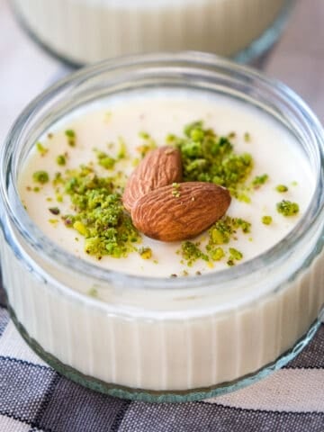 Almond pudding topped with ground pistachios and whole almonds in a glass bowl.