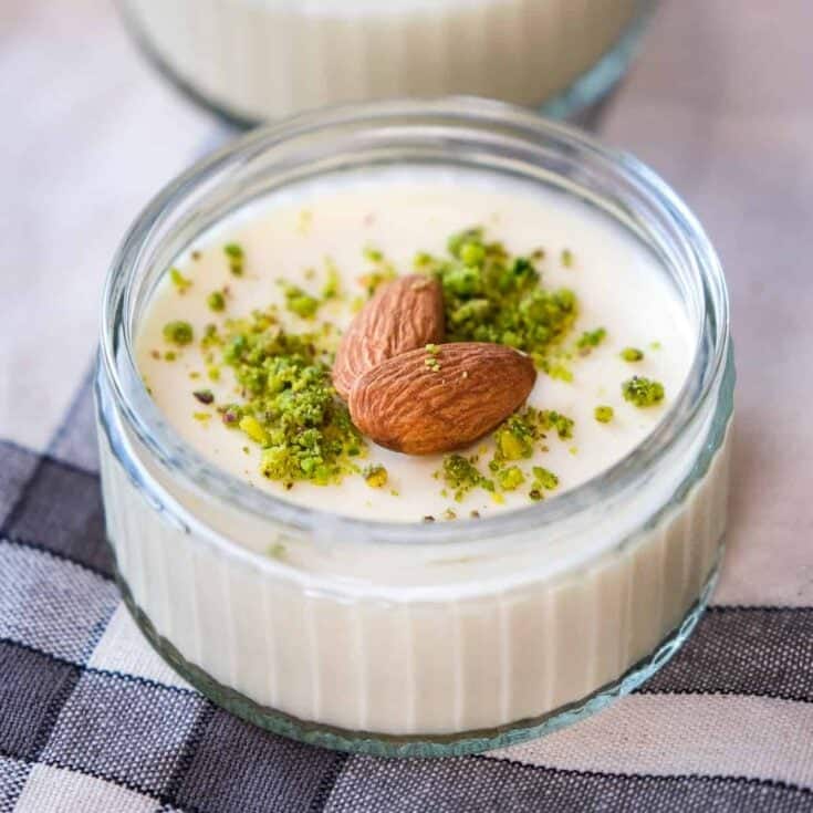 Almond pudding topped with ground pistachios and whole almonds in a glass bowl.