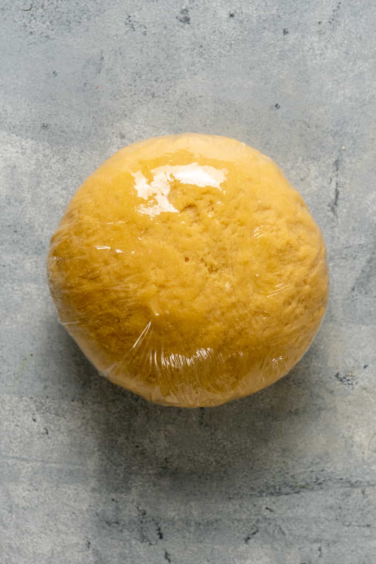 Homemade pasta dough covered with plastic wrap on a grey background.