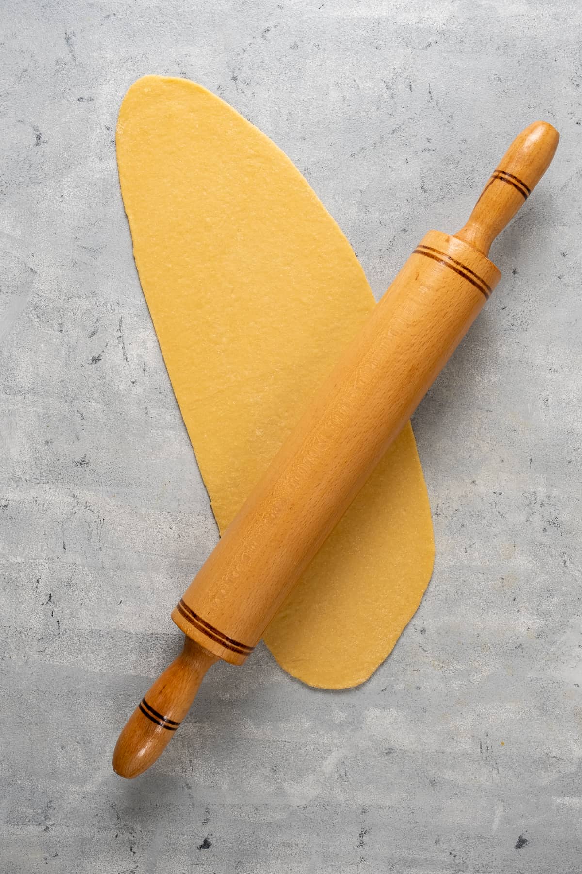 Pasta dough rolled out in an oval shape and a rolling pin on it.