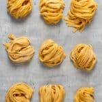 Nested long strips of fresh pasta on a grey background.