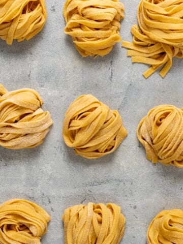 Nested long strips of fresh pasta on a grey background.