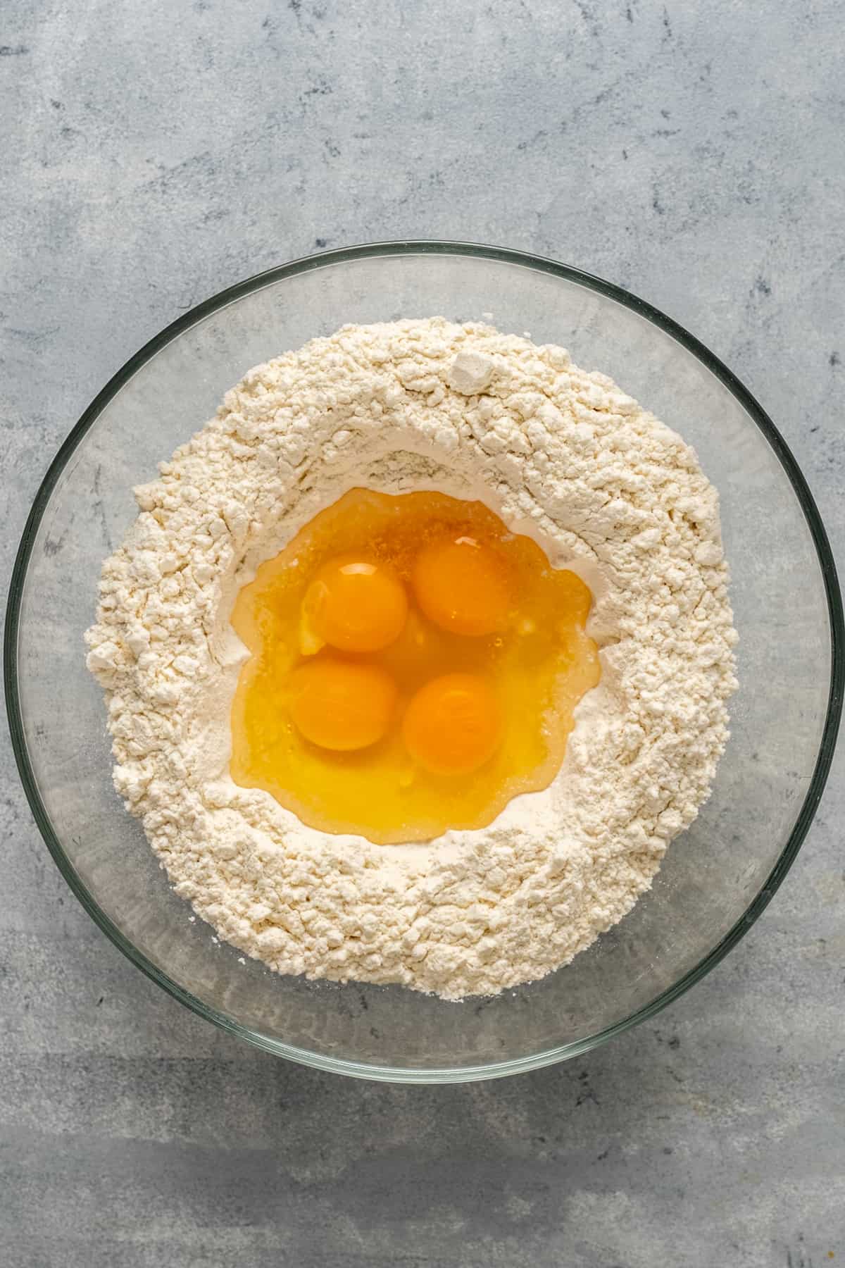 Flour in a glass bowl and eggs in the middle of it.