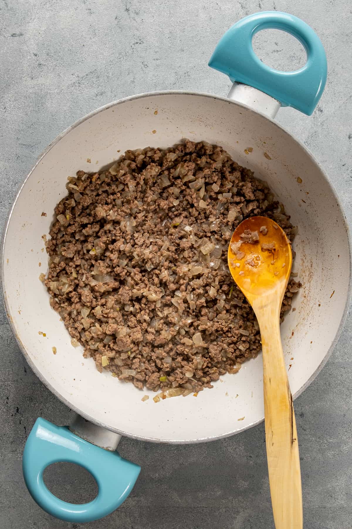 Ground beef cooking in a white pan and a wooden spoon insdie.