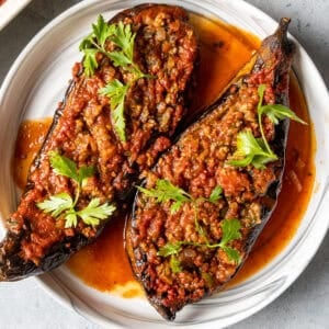 Turkish stuffed eggplants karniyarik garnished with parsley on a white plate.