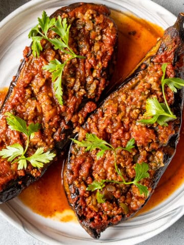 Turkish stuffed eggplants karniyarik garnished with parsley on a white plate.