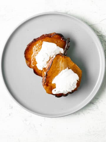 Two cinnamon baked pears topped with clotted cream on a round grey plate.