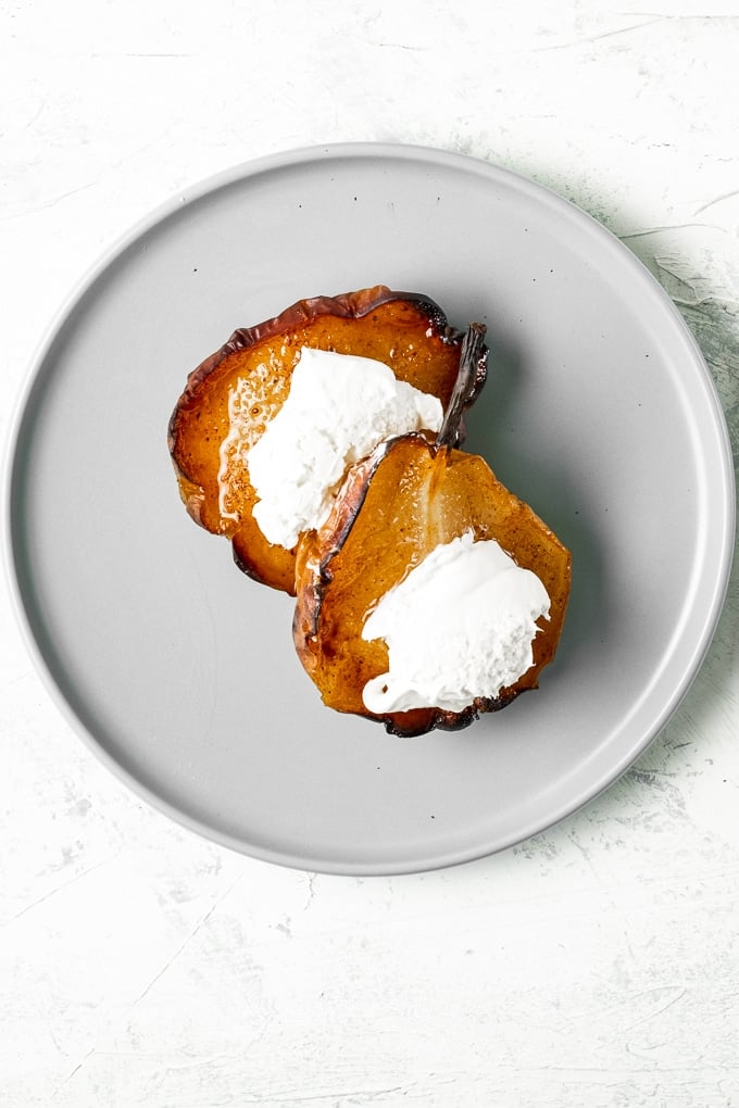 Two cinnamon baked pears topped with clotted cream on a round grey plate.