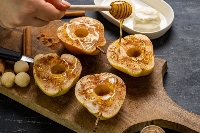 Woman hand drizzling honey over pear halves with a honey dipper.