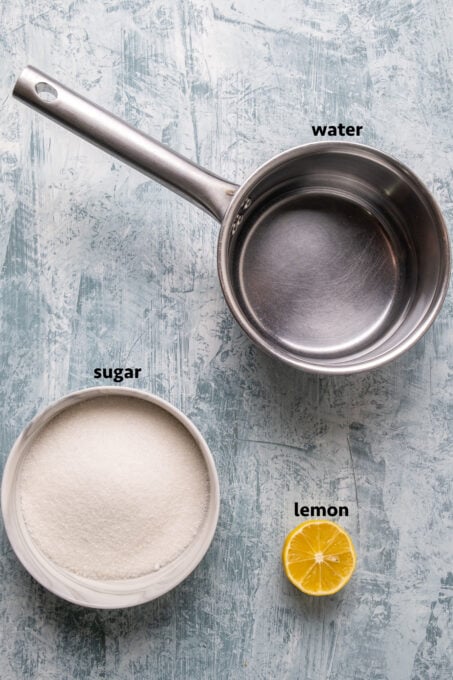Sugar in a bowl, water in a saucepan and a half lemon on a light background.
