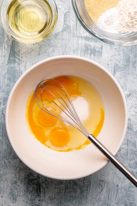 Eggs and sugar in a large white bowl with a hand whisk inside it.