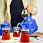 Woman serving Turkish tea in traditional tea glasses from a nostalgic teapot.