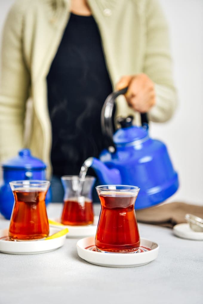 Woman serving Turkish tea in traditional tea glasses from a nostalgic teapot.