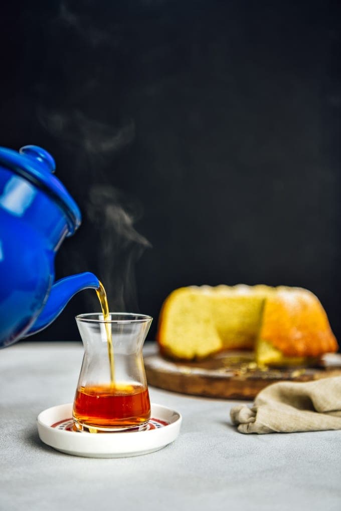 Pouring Turkish tea into a tea glass from a Turkish teapot. Accompanied by a lemon cake.