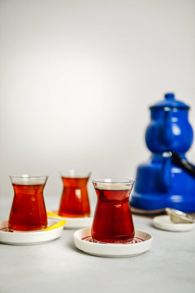 Turkish tea served in three Turkish tea glasses, thin lemon wedges on the side of two. Accompanied by a nostalgic blue tea pot set.