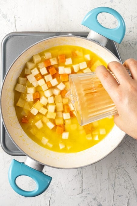 Pouring orange juice over diced celeriac, carrot and quince in a pan.