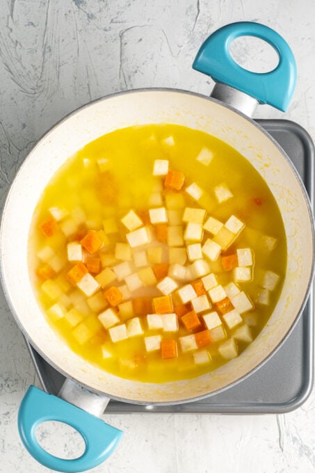 Diced celeriac vegetable, carrot, quince and orange juice in a white pan.
