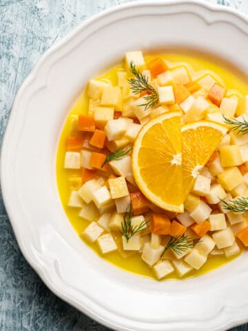 Vegetarian celeriac recipe with carrots, quinces and citrus juice topped with orange wedges in a white round dish.