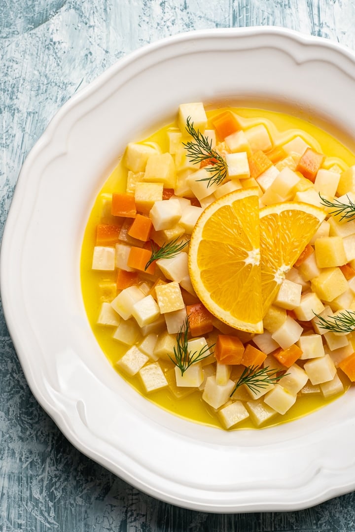 Vegetarian celeriac recipe with carrots, quinces and citrus juice topped with orange wedges in a white round dish.