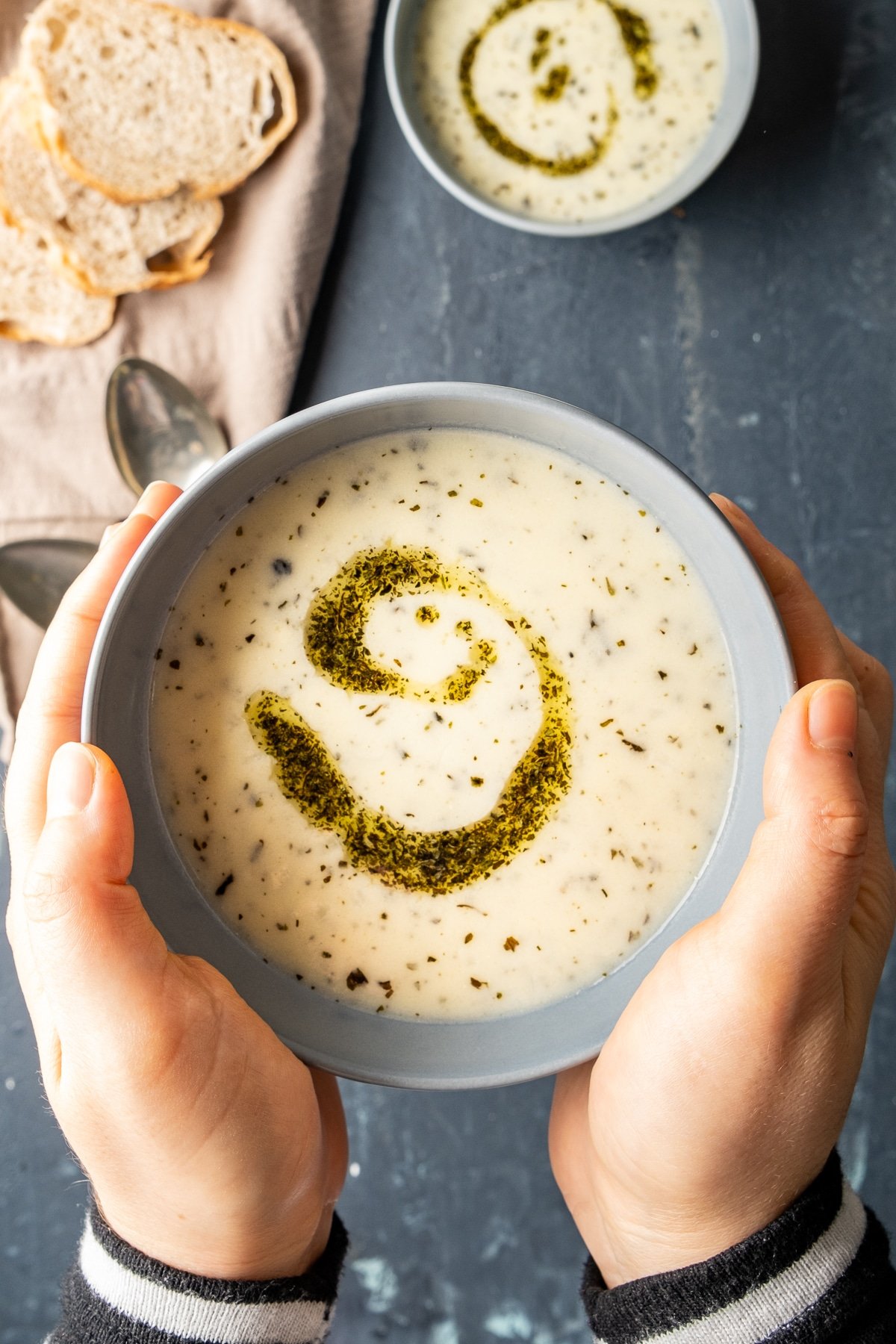 Hands holding a bowl of Turkish yogurt soup.