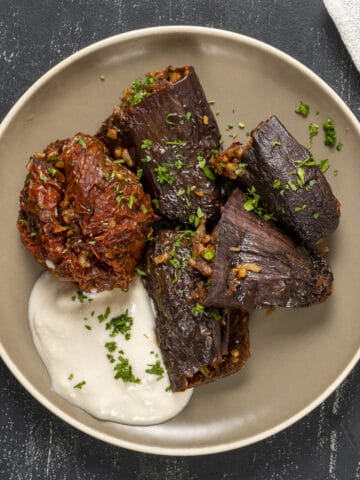 Stuffed dried eggplants and peppers served on a plate with some yogurt on the side.