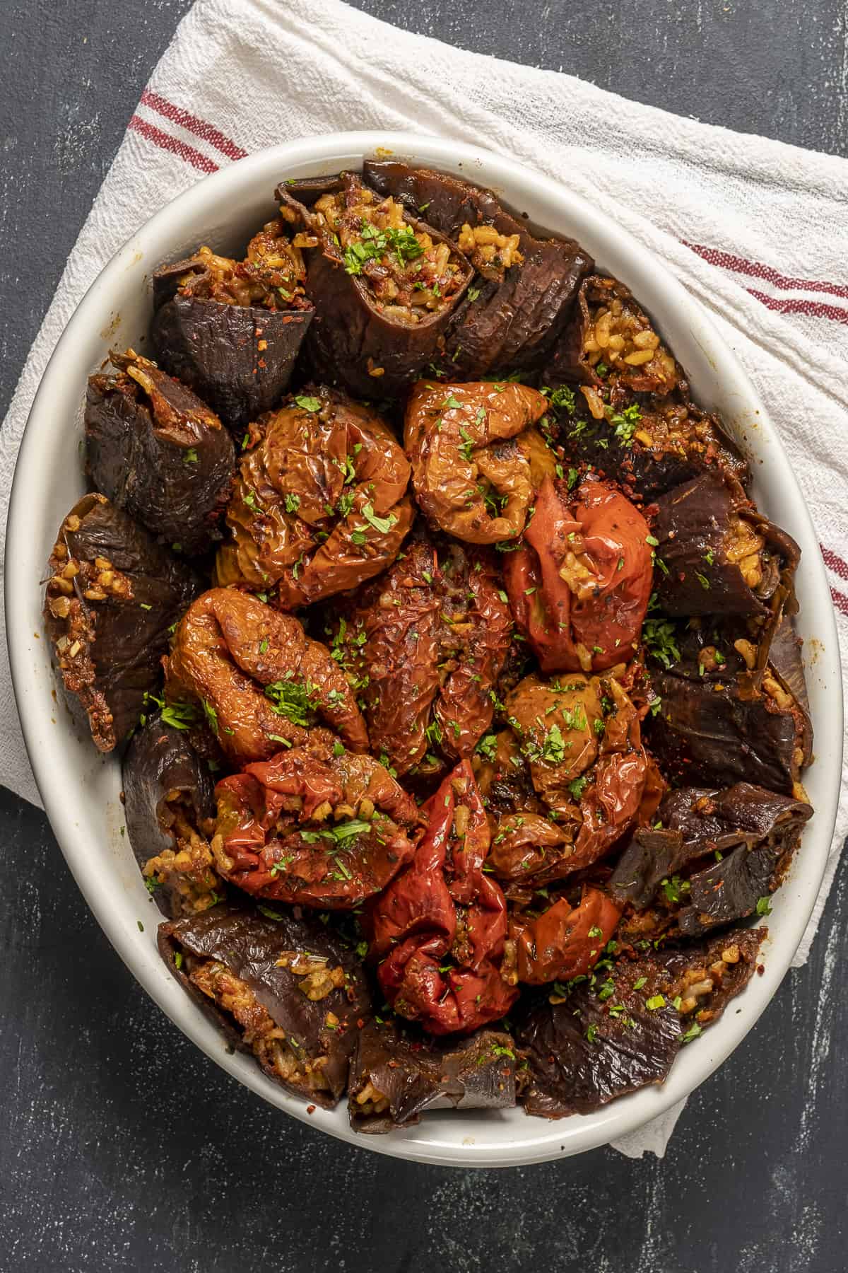 Stuffed dried eggplants and peppers in a white oval baking pan on a white linen.