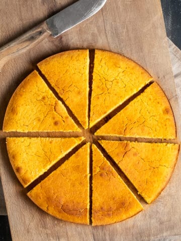 Hot water cornbread baked in a round pan, sliced on a wooden board and a knife on the side.