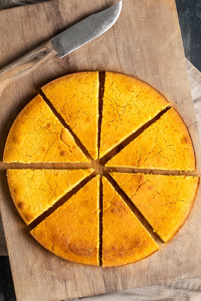 Hot water cornbread baked in a round pan, sliced on a wooden board and a knife on the side.