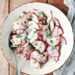 Red radish salad with yogurt, poppy seed and fresh dill dressing in a white bowl.