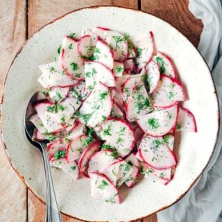 Red radish salad with yogurt, poppy seed and fresh dill dressing in a white bowl.