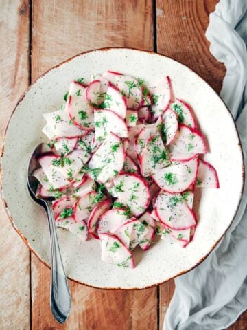 Red radish salad with yogurt, poppy seed and fresh dill dressing in a white bowl.