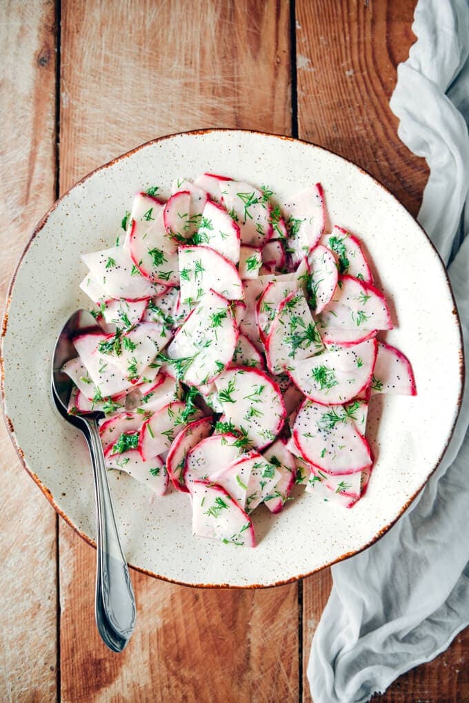 Red radish salad with yogurt, poppy seed and fresh dill dressing in a white bowl.
