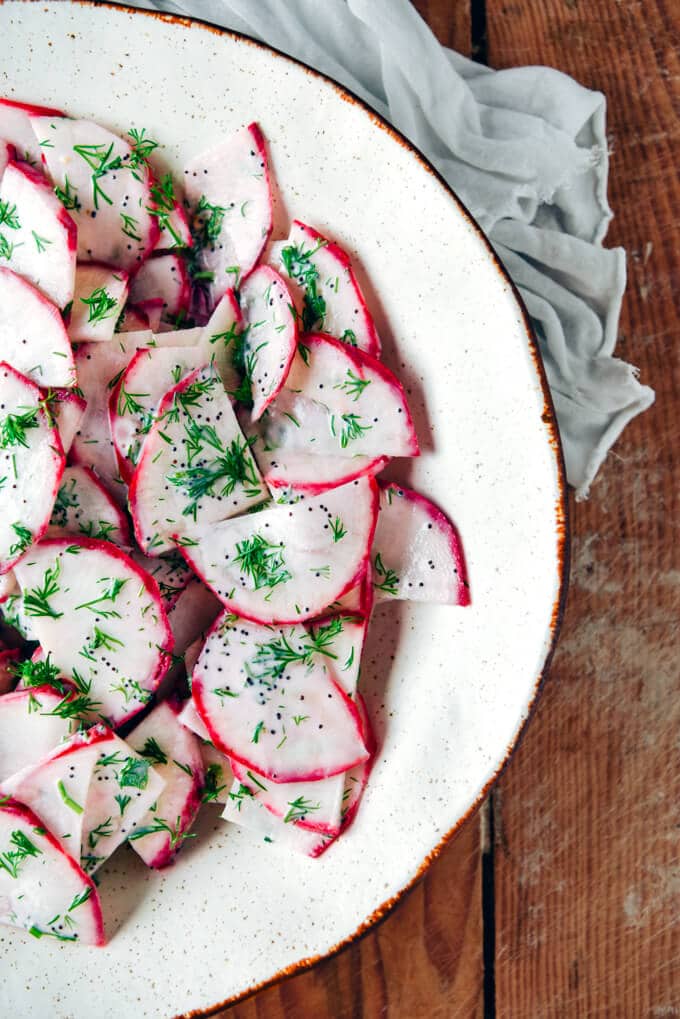 Red radish salad with yogurt, poppy seed and fresh dill dressing in a white bowl.
