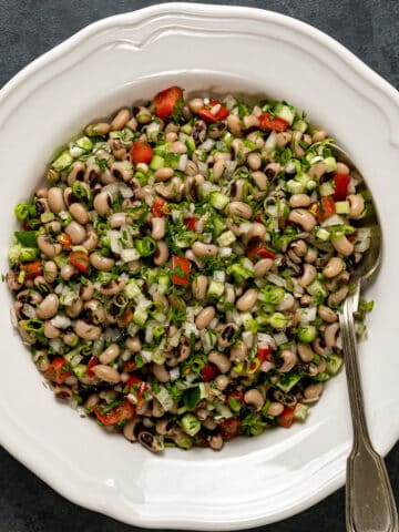 Black eyed pea salad with herbs, onions and sweet red pepper in a white dish and a spoon inside it.