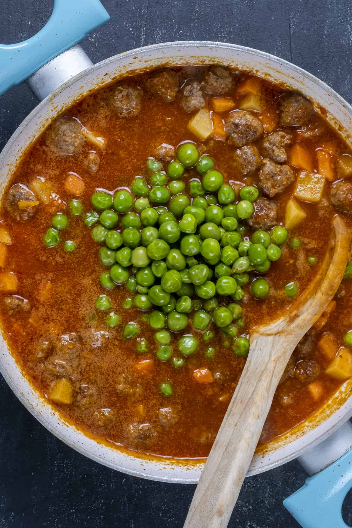 Meatballs, potatoes, carrots and peas with a tomato based stew sauce in a pan.