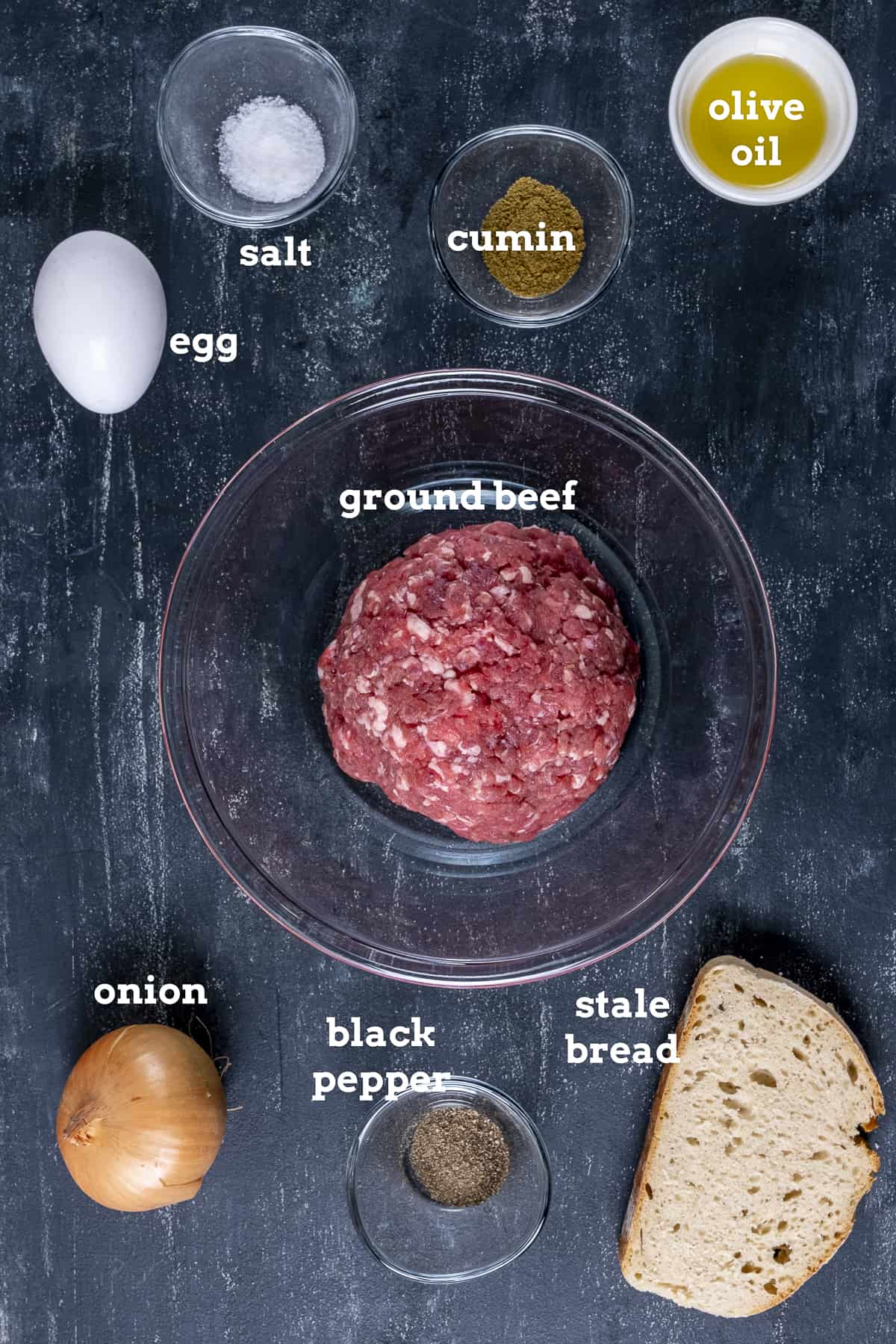 Ground beef, egg, onion, a slice of bread, olive oil, spices on a dark background.