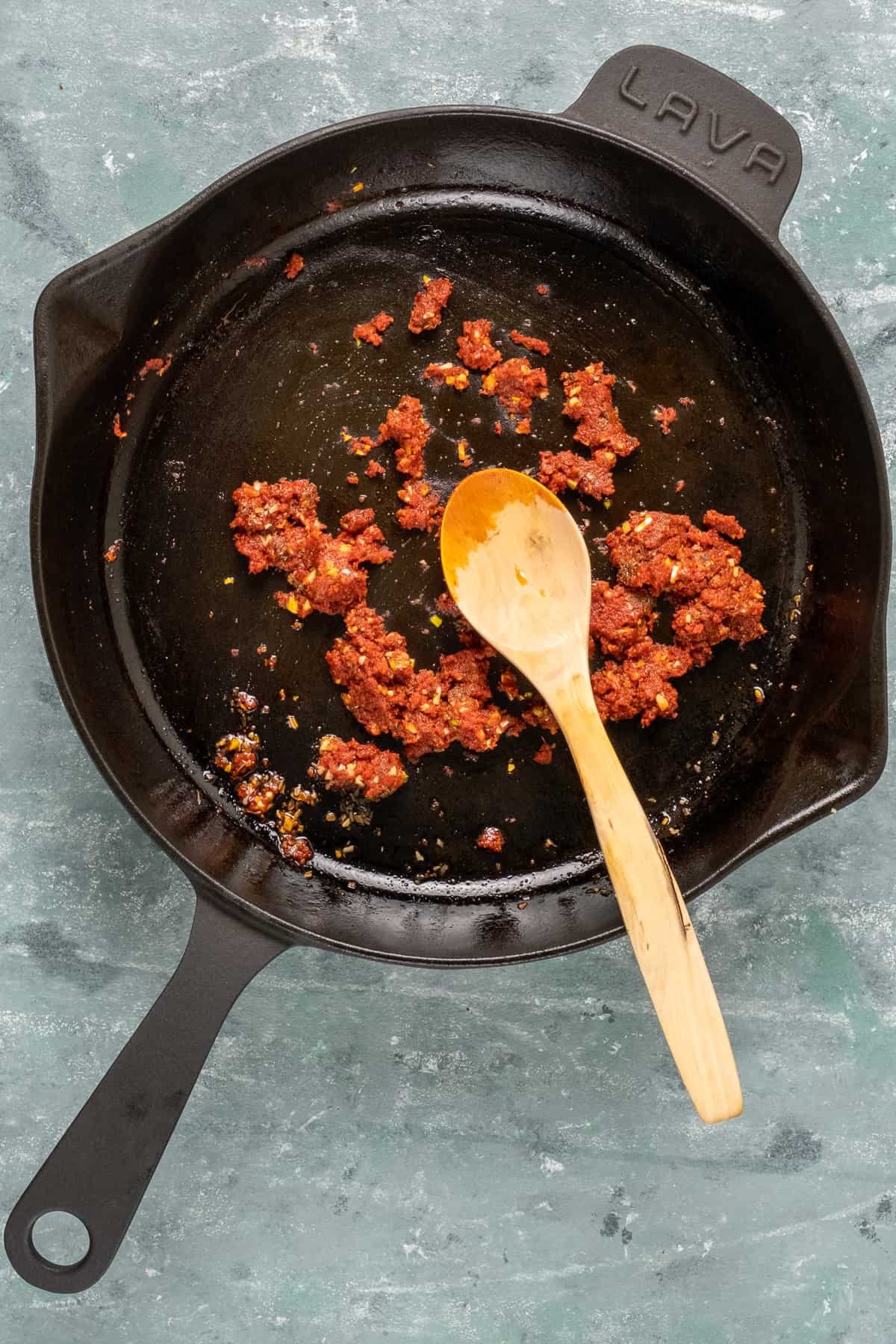 Spices and tomato paste cooking in a cast iron pan with a spoon inside it.