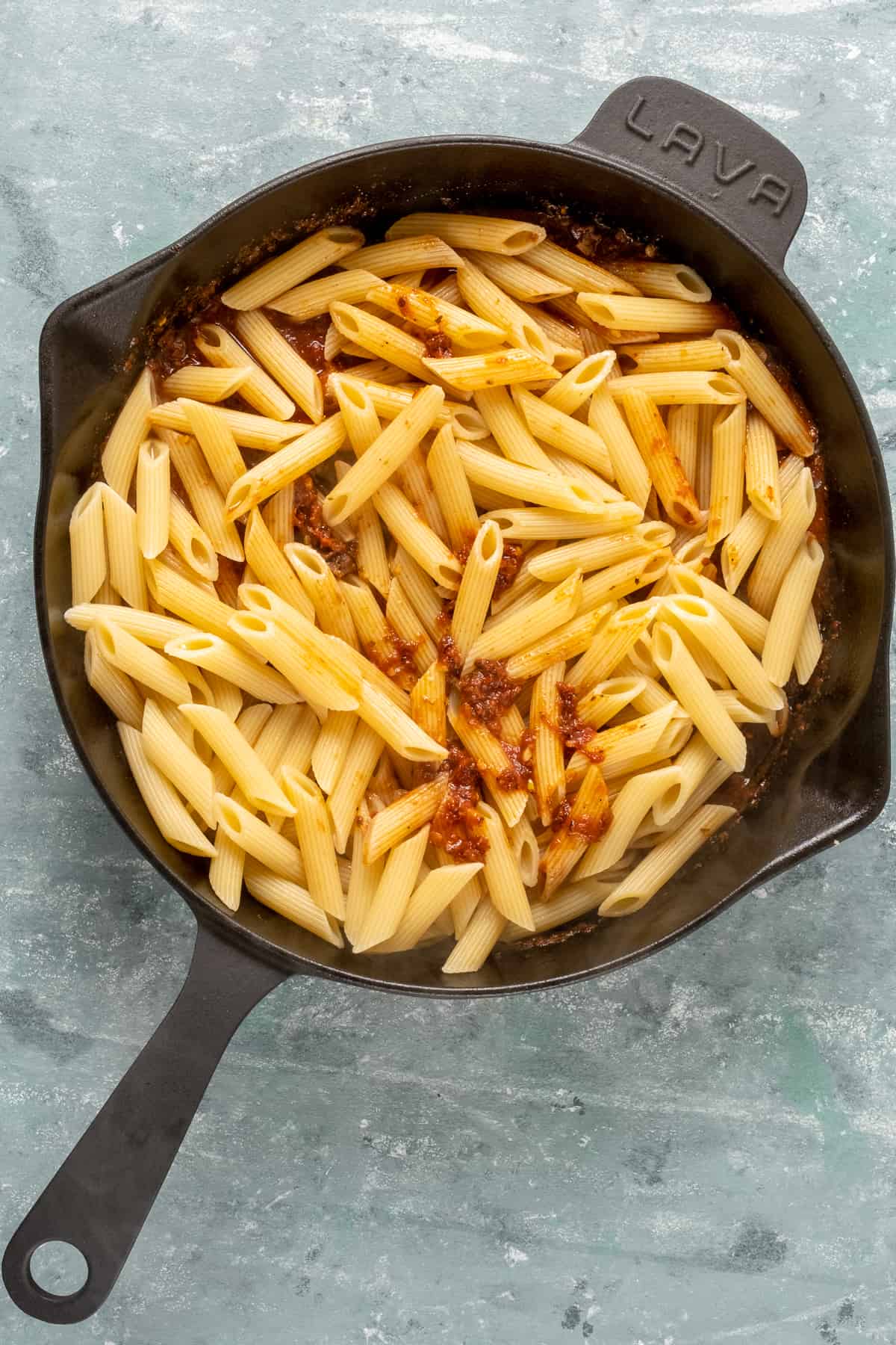 Combining cooked penne pasta with sun-dried tomato sauce in a cast iron skillet.