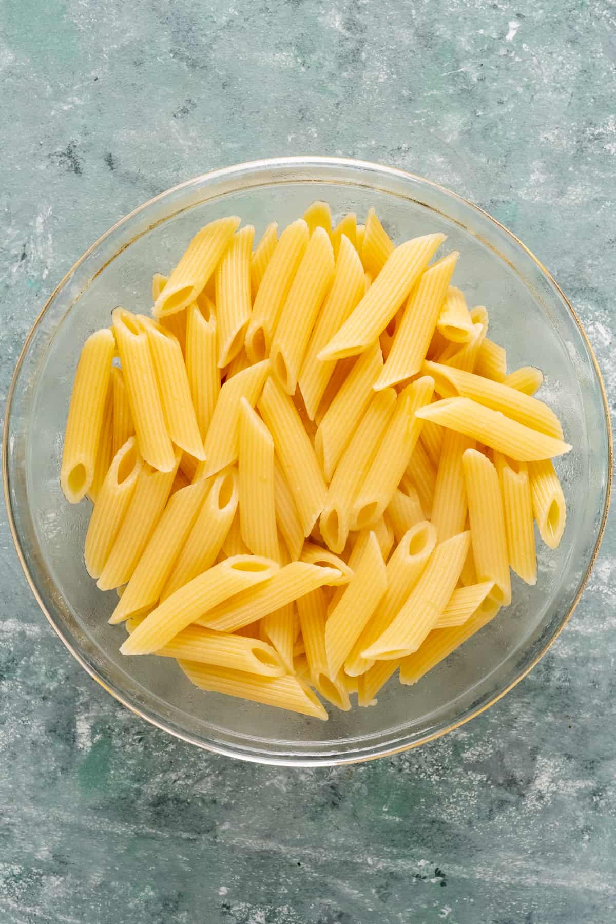 Cooked penne pasta in a glass bowl.