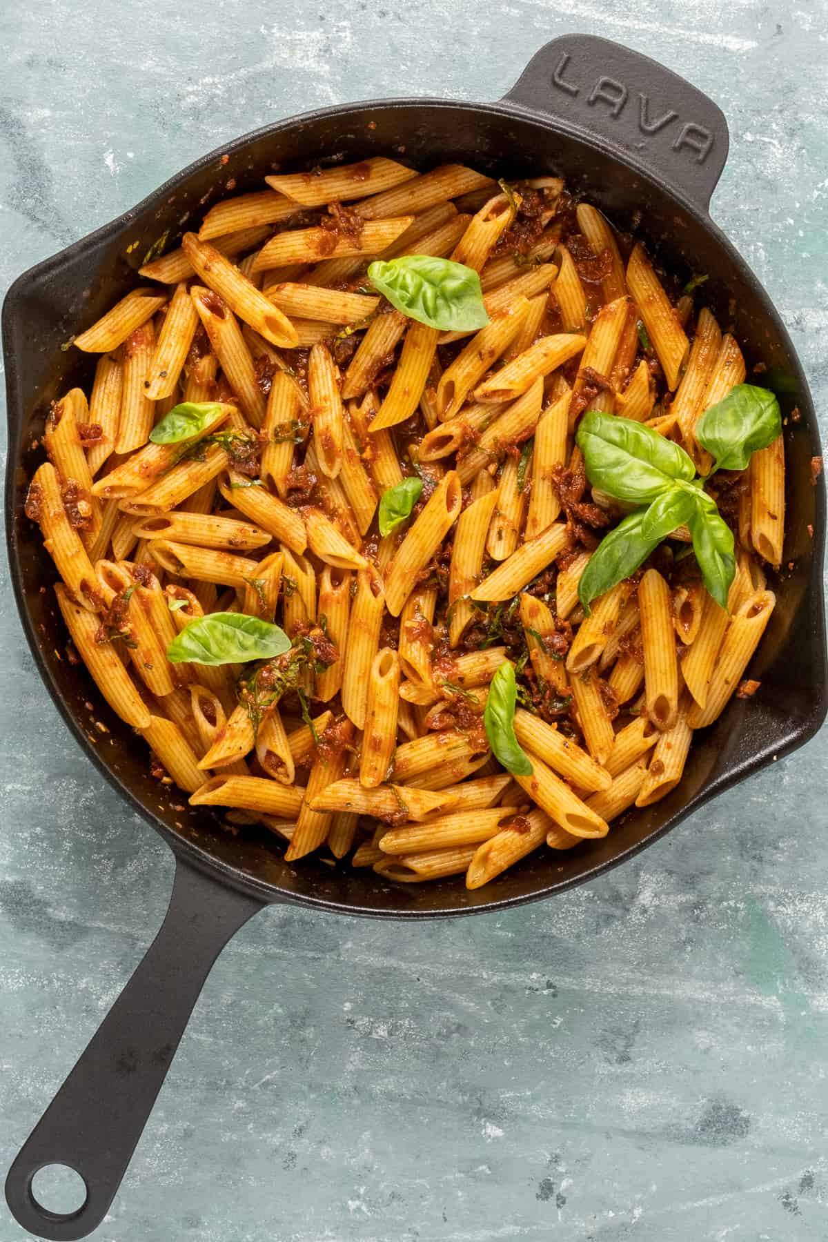 Pasta with sun-dried tomato sauce topped with basil leaves in a cast iron skillet.