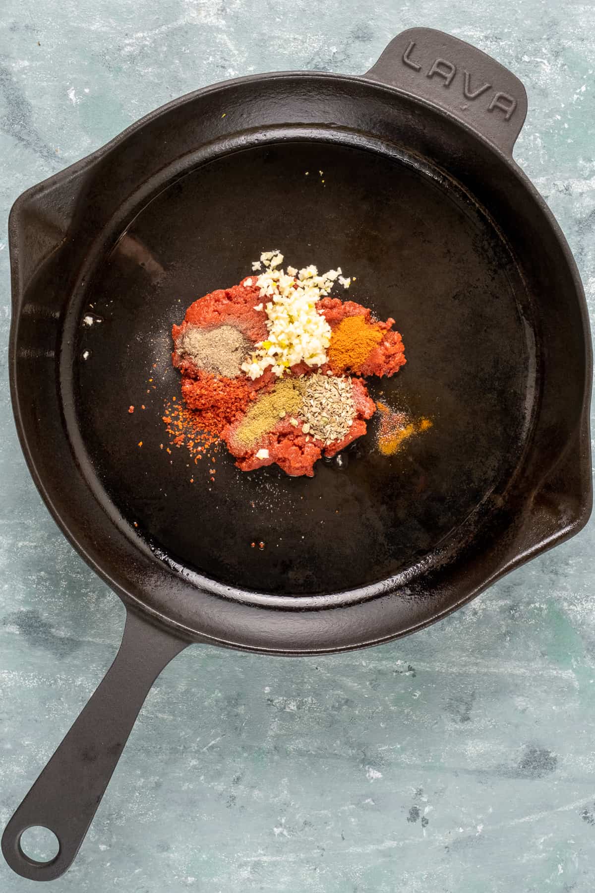 Spices, tomato paste and minced garlic in a cast iron skillet.