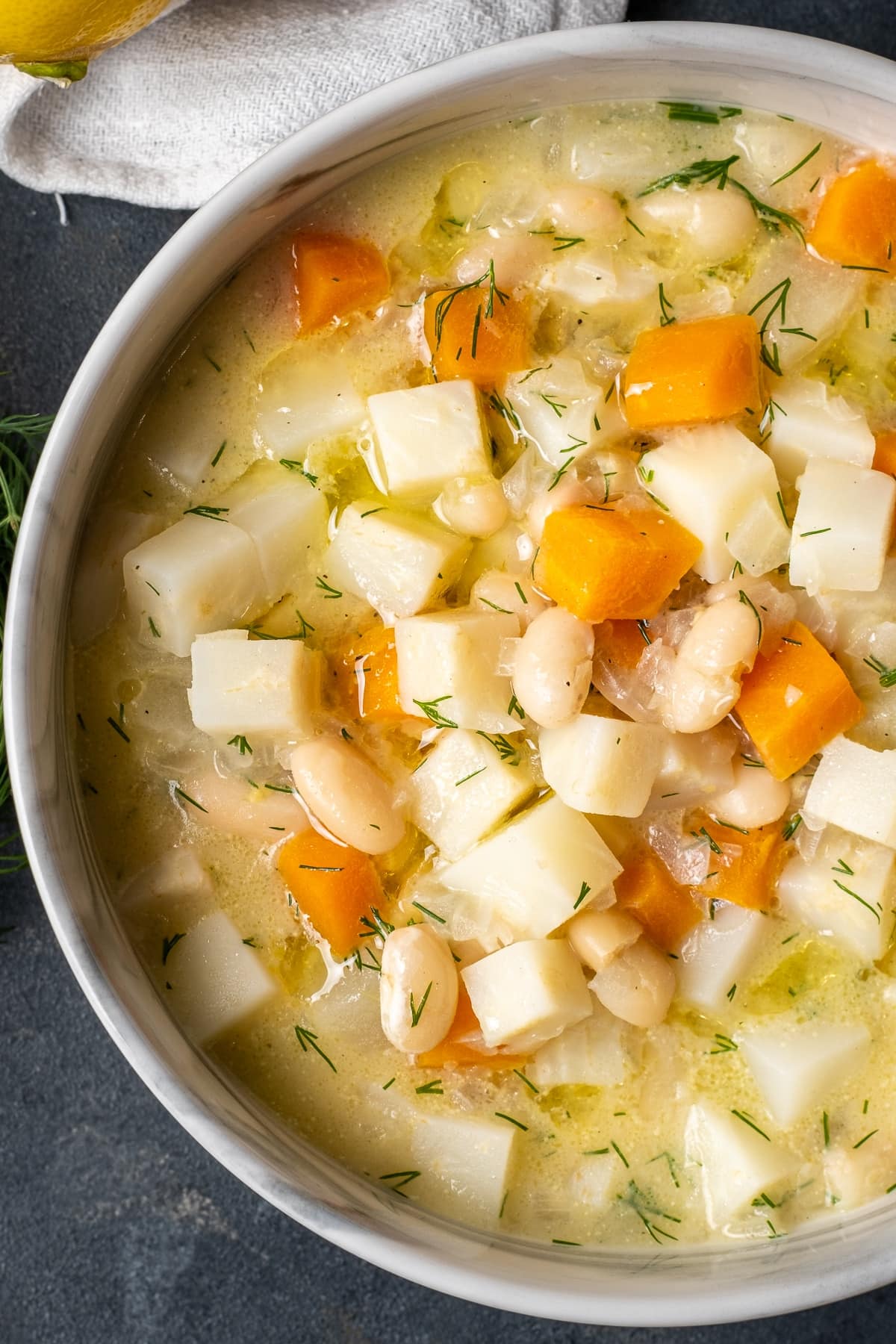 Celery root soup with apples, carrots and beans in a bowl on a dark background.