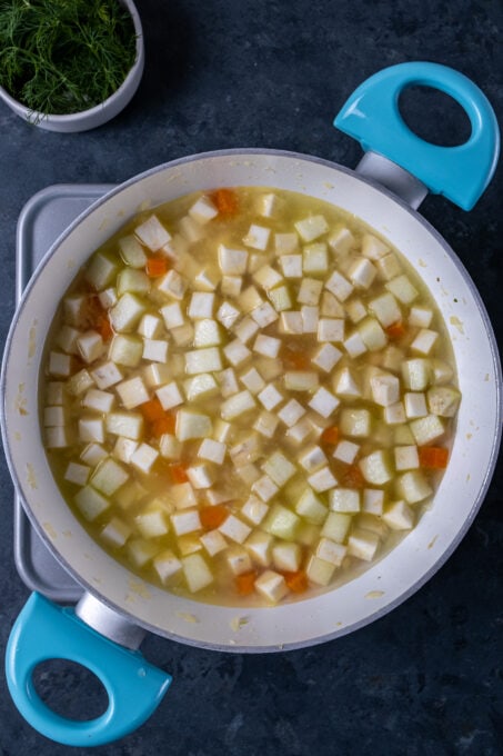 Diced celery roots, carrots, apples and water in a white pan.