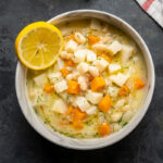 Celery root and bean soup in a white bowl with a lemon slice on the side.