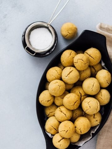 Mini tahini cookies in a black oval bowl photographed on a grey background.