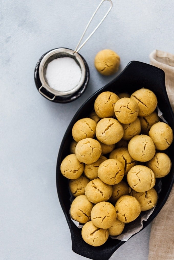 Mini tahini cookies in a black oval bowl photographed on a grey background. 